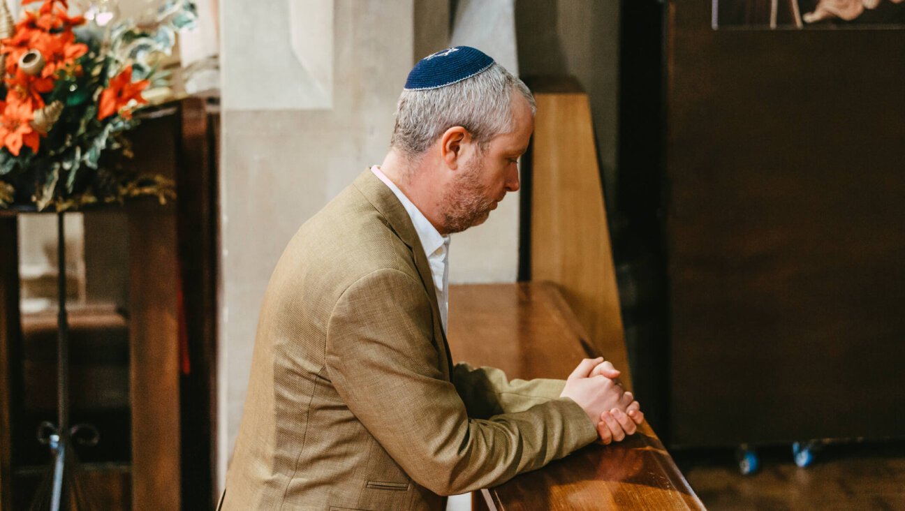 Portrait of a Jewish man kneeling and praying in the synagogue during Yom Kippur. The man is wearing a yarmulke on his head as he sits alone in the synagogue.