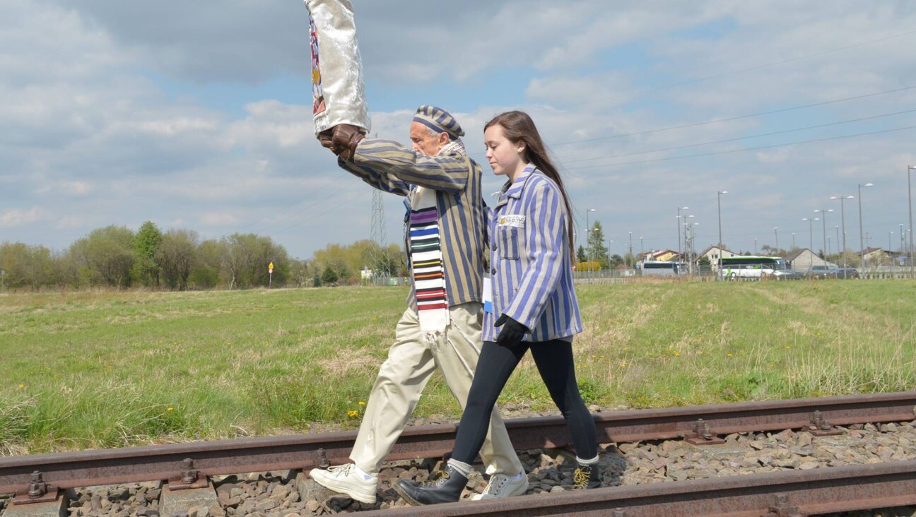 A Holocaust survivor holds a Torah scroll aloft as he walks with a young woman down the train tracks leading from Auschwitz to Birkenau.