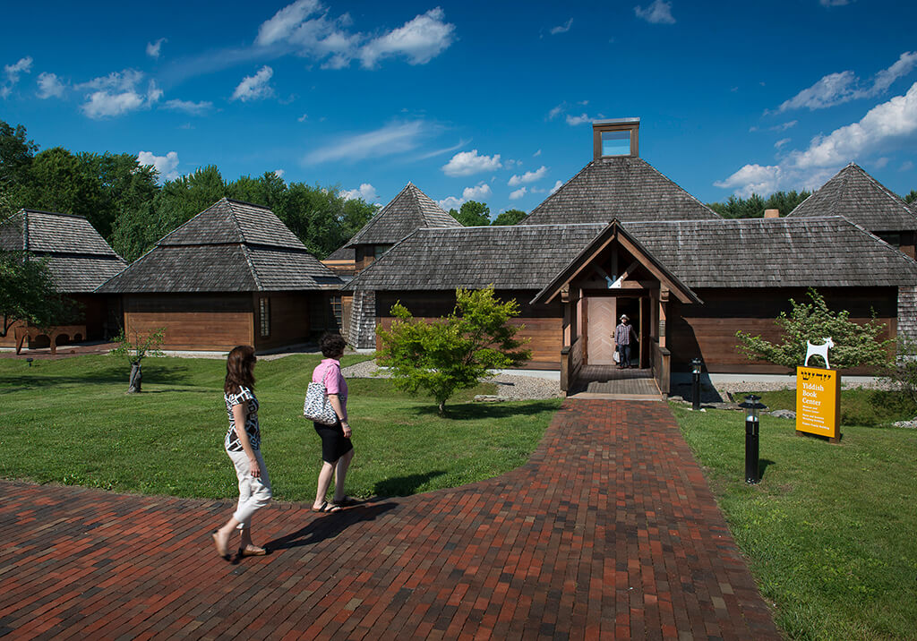 The exterior of the Yiddish Book Center, a campus of low brown buildings with a brick path and green lawn.