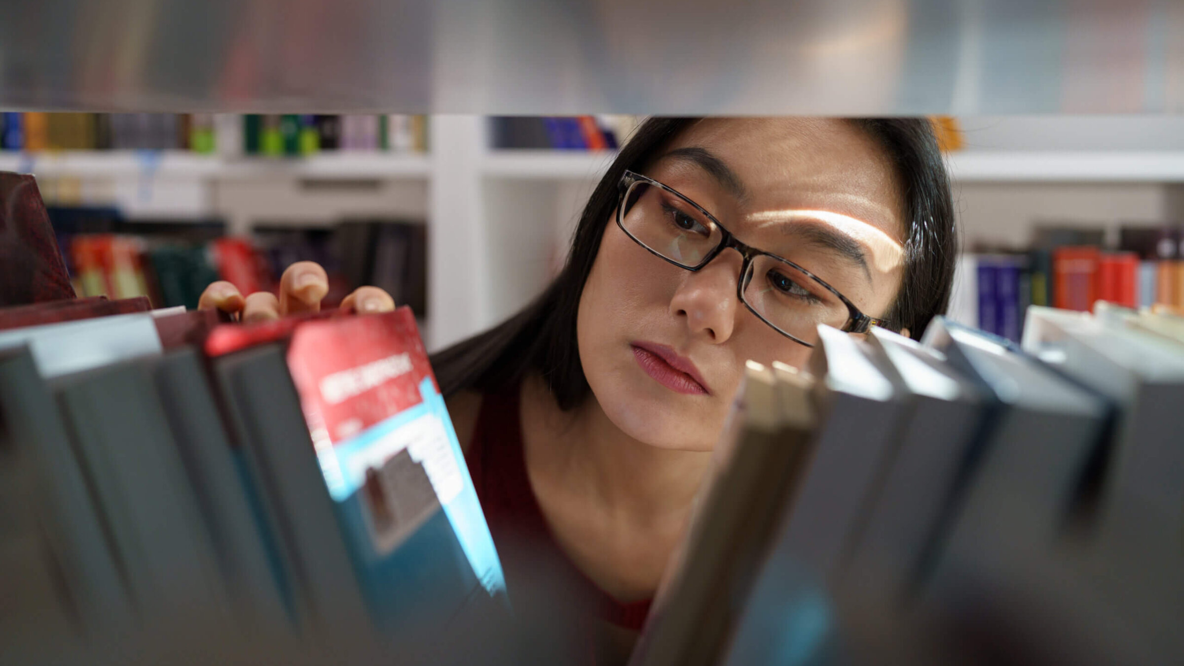 A young woman examines a bookshelf.