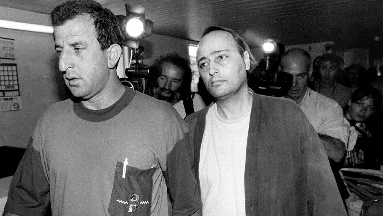 Eddie Antar, right, once known as “Crazy Eddie,” New York’s electronics king, is led by an Israeli police detective in Petah Tiqva, Israel, June 25, 1992. (Sven Nackstrand/AFP via Getty Images)