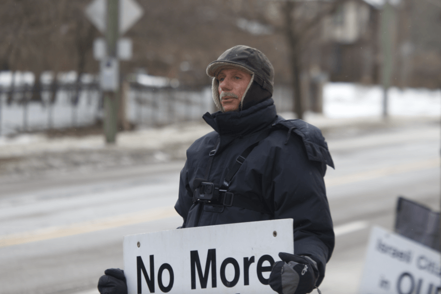 Henry Herskovitz protesting outside Beth Israel Congregation in Ann Arbor, Michigan, in December 2021. He holds a poster that  says "No More Holocaust Movies." 