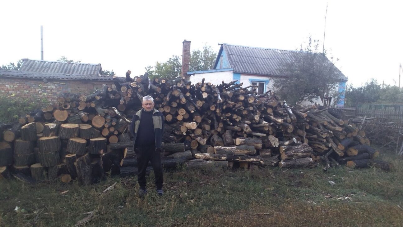 An elderly Jewish man in the Dnipro region of Ukraine stands before a delivery of firewood made by JDC as part of an effort to support Ukrainian Jews in advance of a punishing winter. (Courtesy of the JDC)