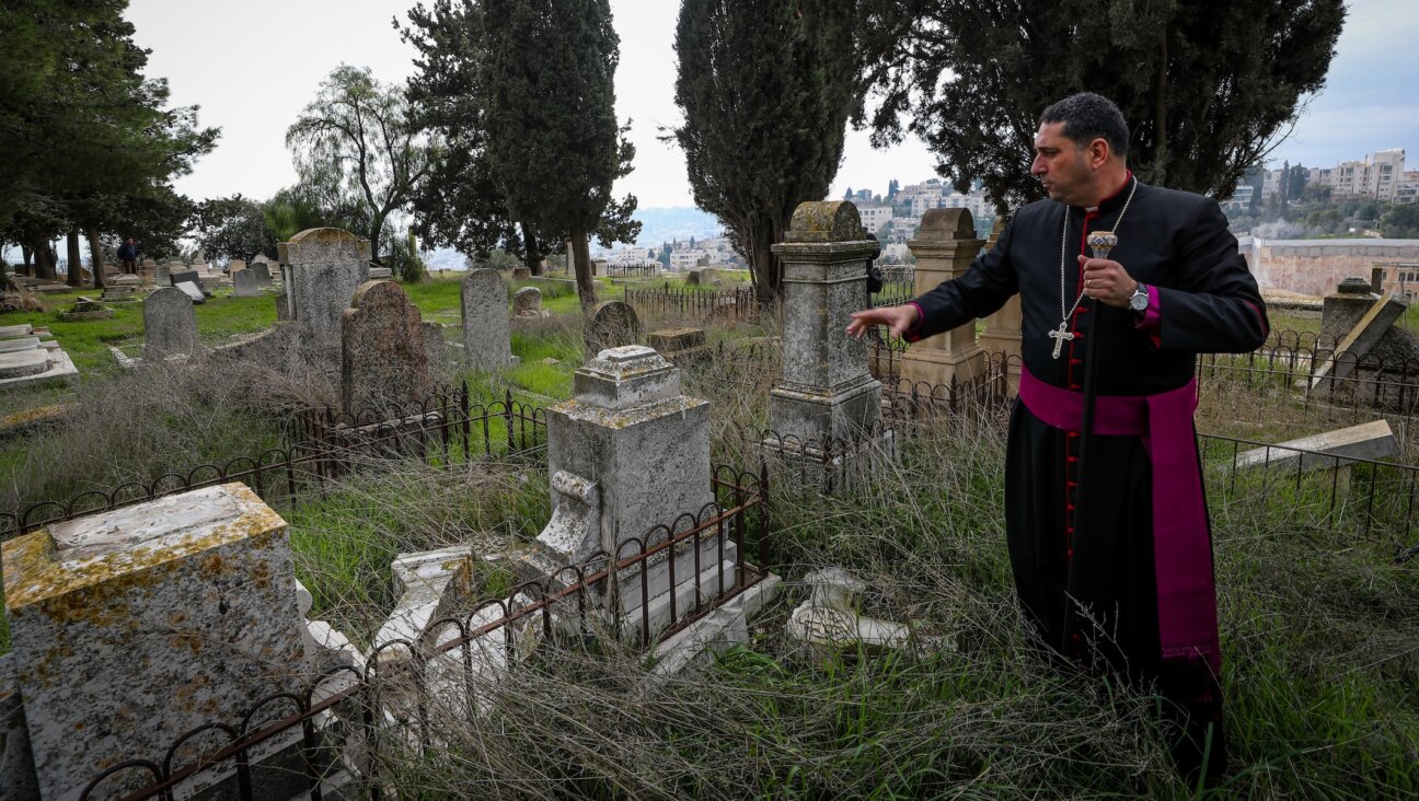 A priest shows a gravestone allegedly vandalized by Jewish men in the Christian cemetery on Mount Zion, in the Old City of Jerusalem, January 4, 2023. (Jamal Awad/Flash90)