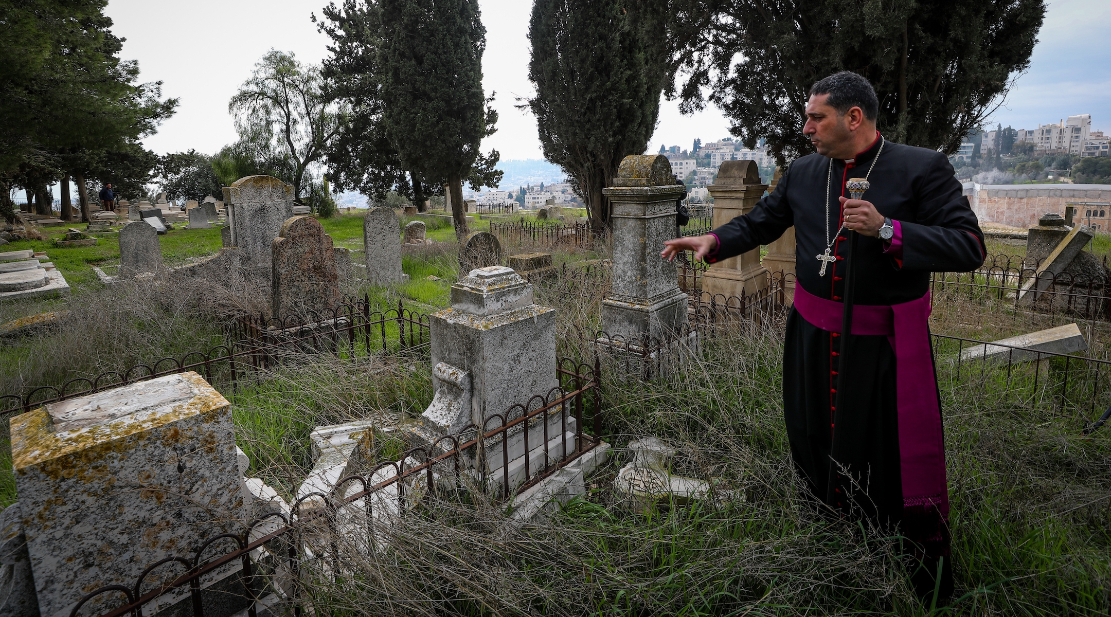 A priest shows a gravestone allegedly vandalized by Jewish men in the Christian cemetery on Mount Zion, in the Old City of Jerusalem, January 4, 2023. (Jamal Awad/Flash90)