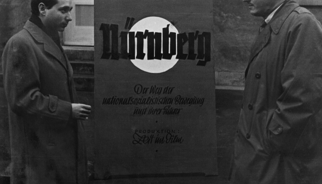 Stuart Schulberg, left, by a poster of his 1948 film <i>Nuremberg: Its Lesson for Today,</i> which premiered in Stuttgart, Germany, but never had a proper American release in his lifetime.