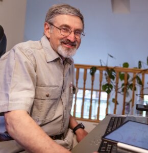 Photo of Waxman, a white man with gray hair and glasses, sitting at his desk, smiling brightly toward the camera.