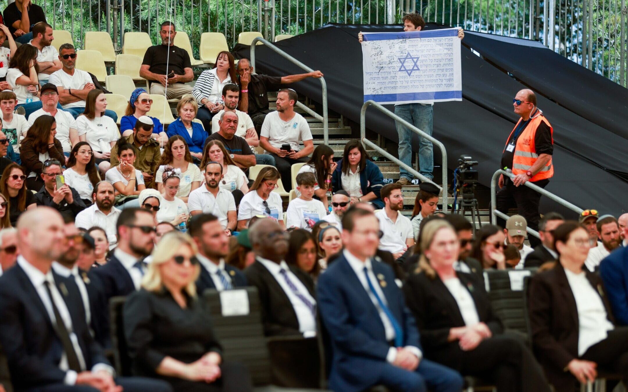 A man holds an Israeli flag with signatures from the Israeli Declaration of Independence during a silent protest against Israeli Prime Minister Benjamin Netanyahu at a state memorial ceremony for victims of terror, in Mount Herzl military cemetery, Jerusalem, April 25, 2023. (Erik Marmor/Flash90)