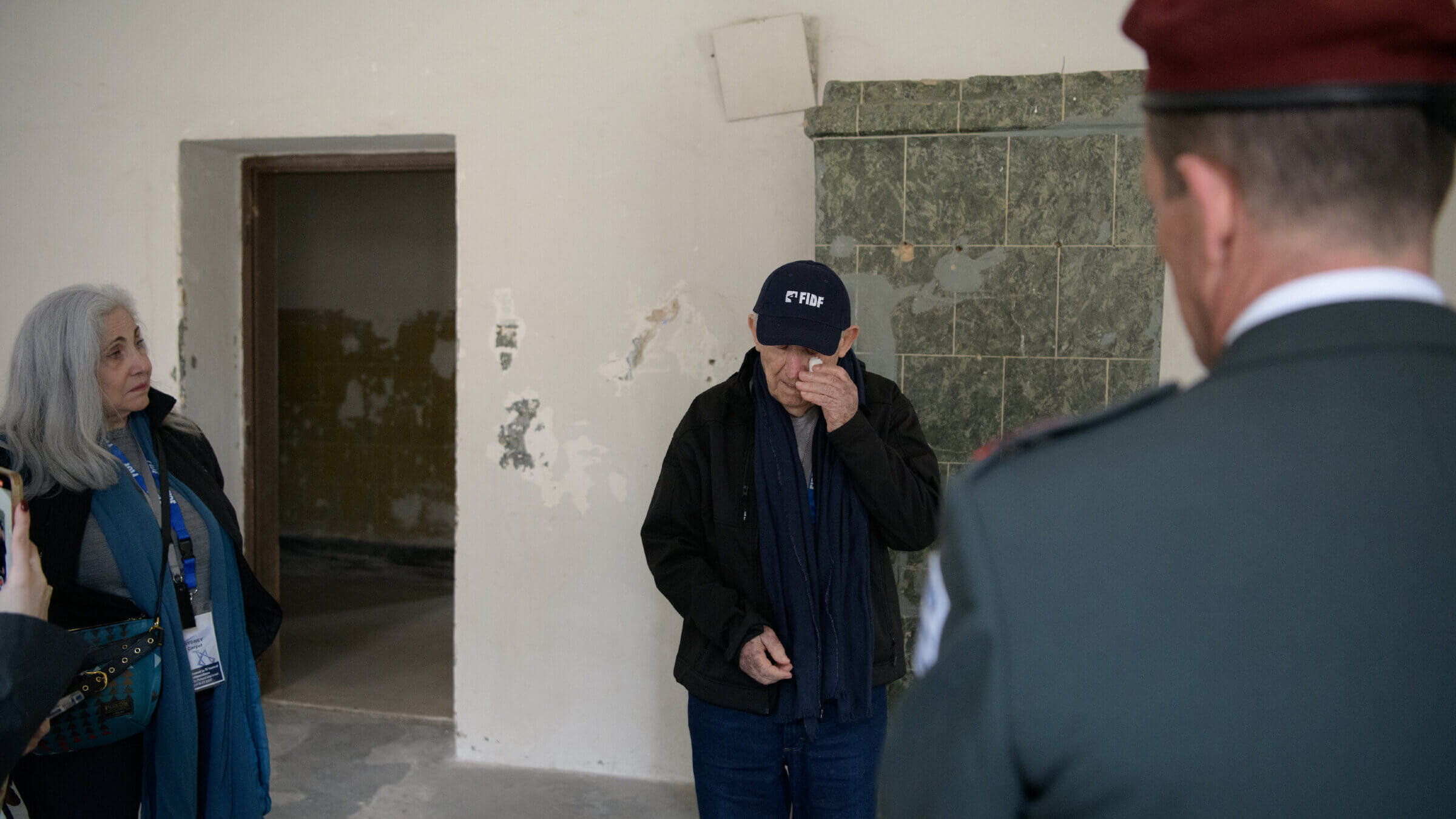 David Schaecter inside Block 8 at Auschwitz-Birkenau on April 24, 2023. His wife, Sydney Carpel, is at left and an IDF officer faces them.