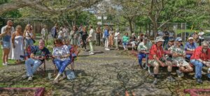 A crowd of several dozen people waits at a municipal park for the marker dedication ceremony to begin.