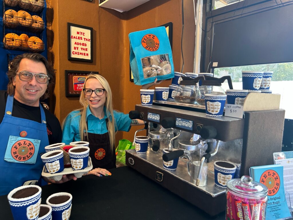 Man and woman smile next to coffee maker and felted blue-and-white greek diner coffee cups.