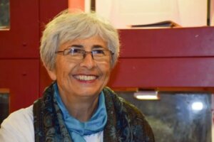 White woman with short gray hair smiling with a scarf on