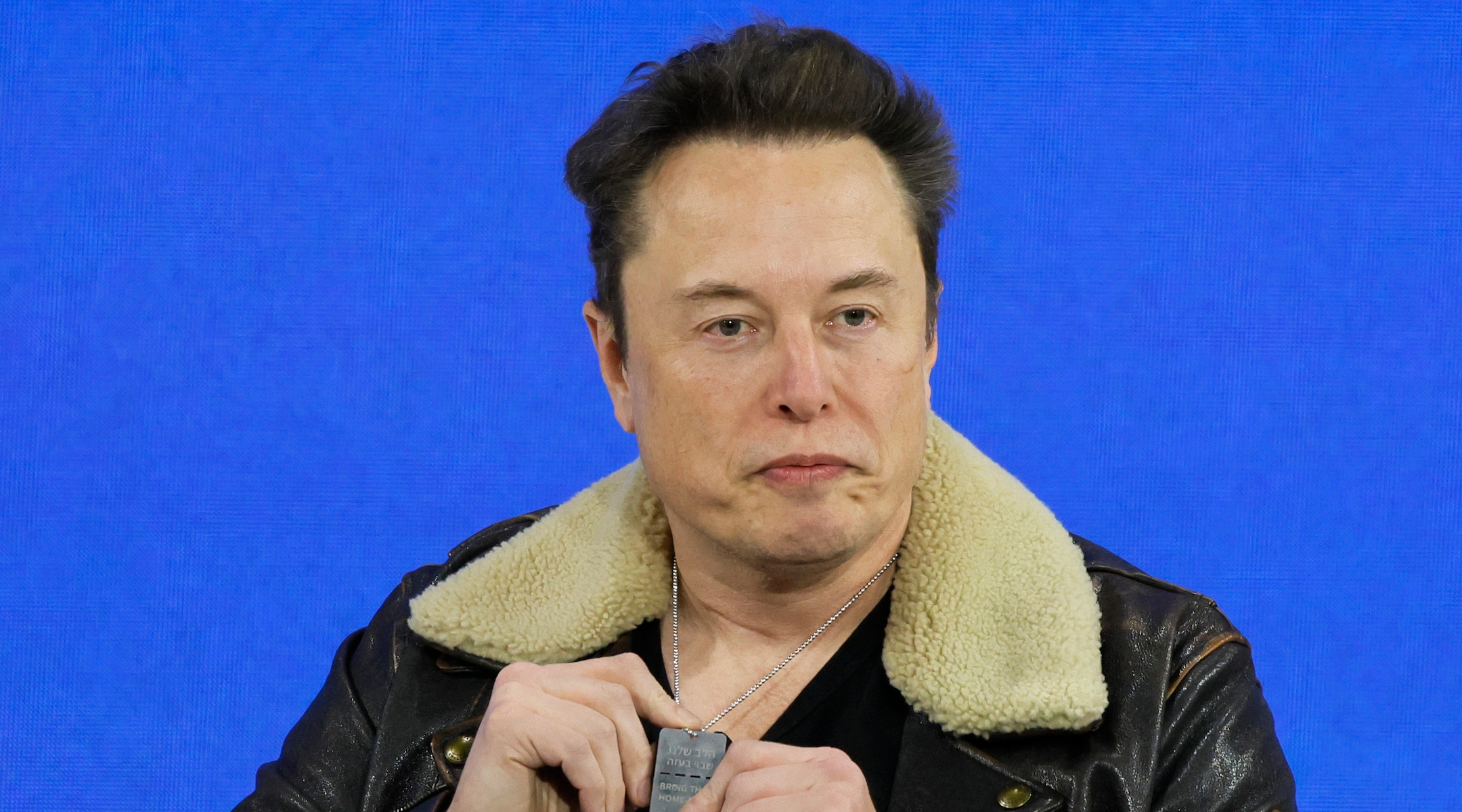 Elon Musk holds up a pendant from Israel that says “Bring Them Home” as he speaks during the New York Times annual DealBook summit on November 29, 2023 in New York City. (Michael M. Santiago/Getty Images)