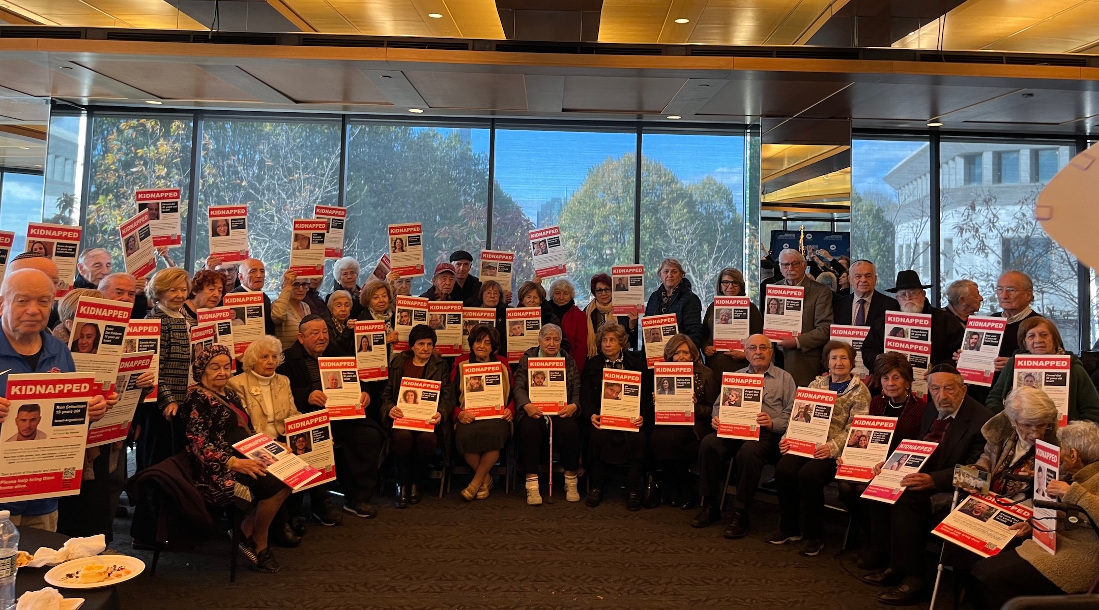 A group of Holocaust survivors pose with posters of the hostages that were kidnapped by Hamas at the Museum of Jewish Heritage: A Living Memorial to the Holocaust, Nov. 1, 2023. (Julia Gergely)