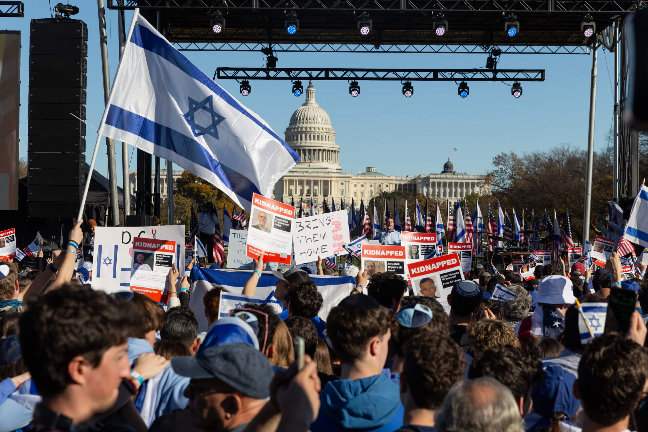 The U.S. Capitol stands behind the stage while a crowd of people holds signs and flags in support.