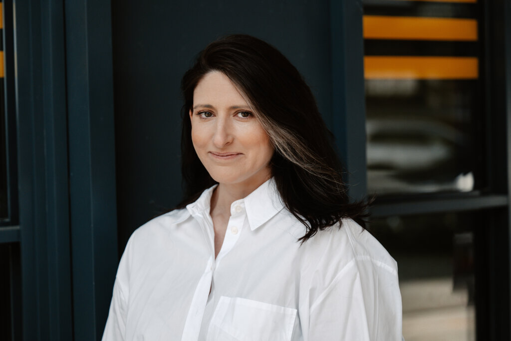 Woman in white button down shirt smiles at camera with black background