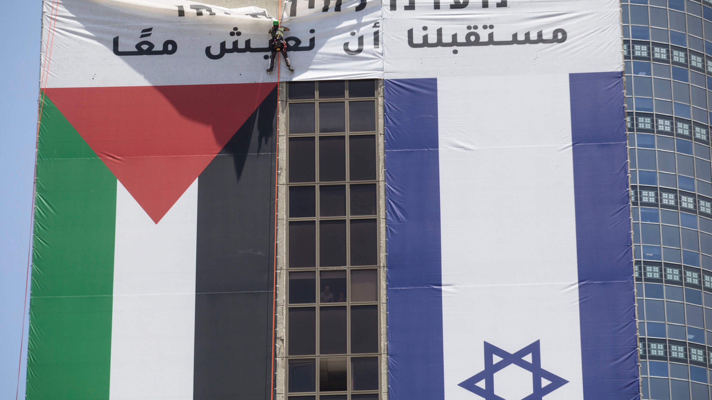 A man removes the Palestinian flag from a building after it was displayed by a left wing group in support of coexistence, June 1, 2022 in Ramat Gan, Israel. 