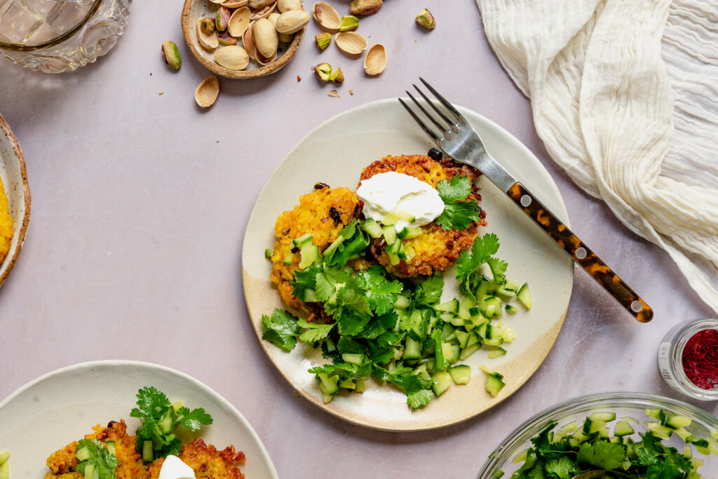 Three golden brown pancakes on a plate with a fork on it, topped with sour cream and lots of scallions.