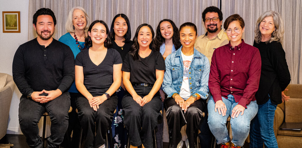 Ten people pose in two rows for a photo with beige curtains behind them.