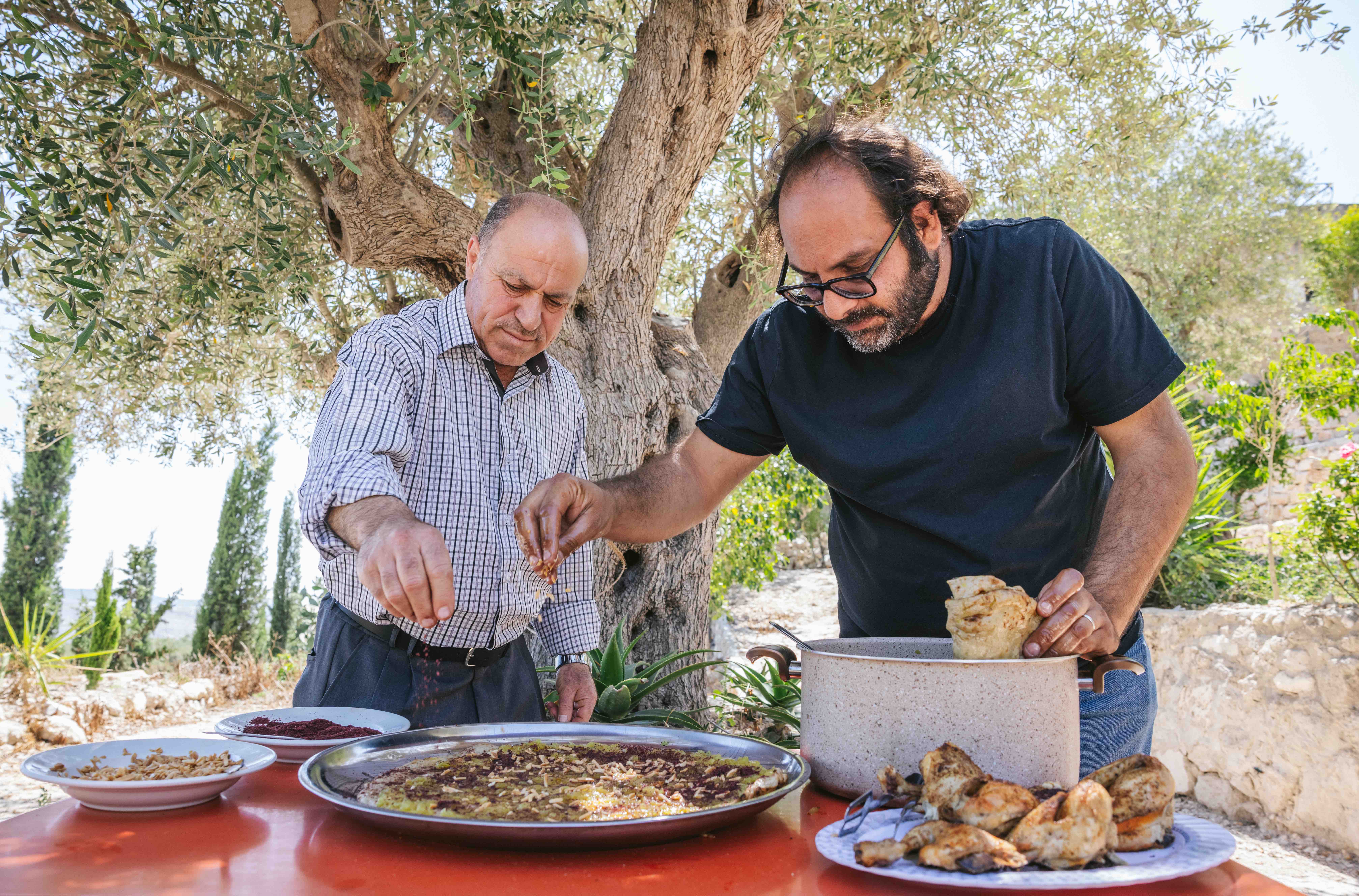 Fadi Kattan, right, prepares musakhan, a dish of flatbread and onion confit covered in purple sumac and olive oil, with Abu Mohammad, left, a restaurant owner in the West Bank village of Sebastia. 