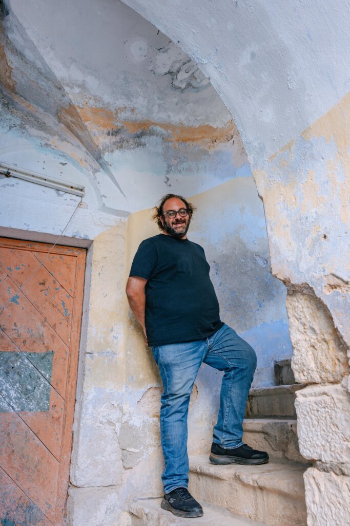 A man stands smiling under an old plaster arch.