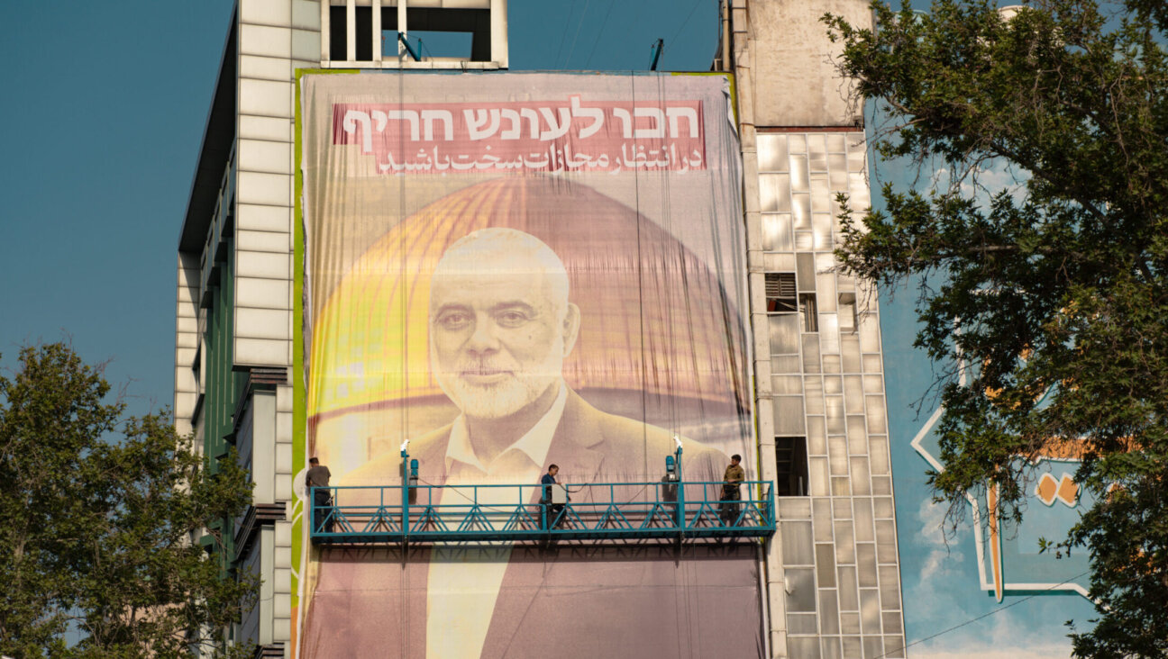 Workers hang a billboard bearing a portrait of Ismail Haniyeh with a slogan in Hebrew and Farsi saying “Expect severe punishment” at Palestine Square in Tehran on July 31, 2024 (Hossein Beris/Middle East Images/AFP via Getty Images)