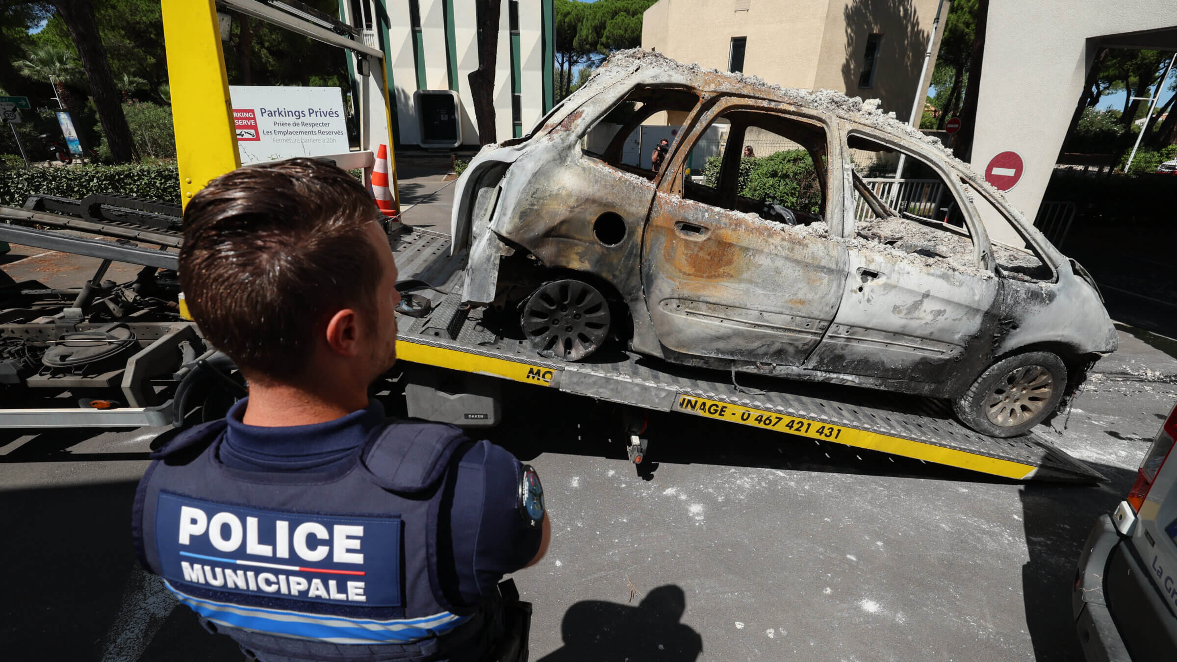 A police officer stands in front of a burnt car being moved on the bed of a towing vehicle in the seaside resort of La Grande Motte, near the Beth Yaacov synagogue.