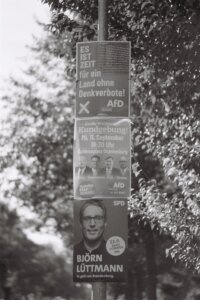 A stack of campaign posters on a street lamp post for Brandenburg's state election. The top poster for AfD says "ES IST ZEIT für ein Land ohne Denkverbote!"