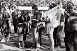 A teenager in a crowd at a protest wears a tote bag over their shoulder that says "FCK AFD"