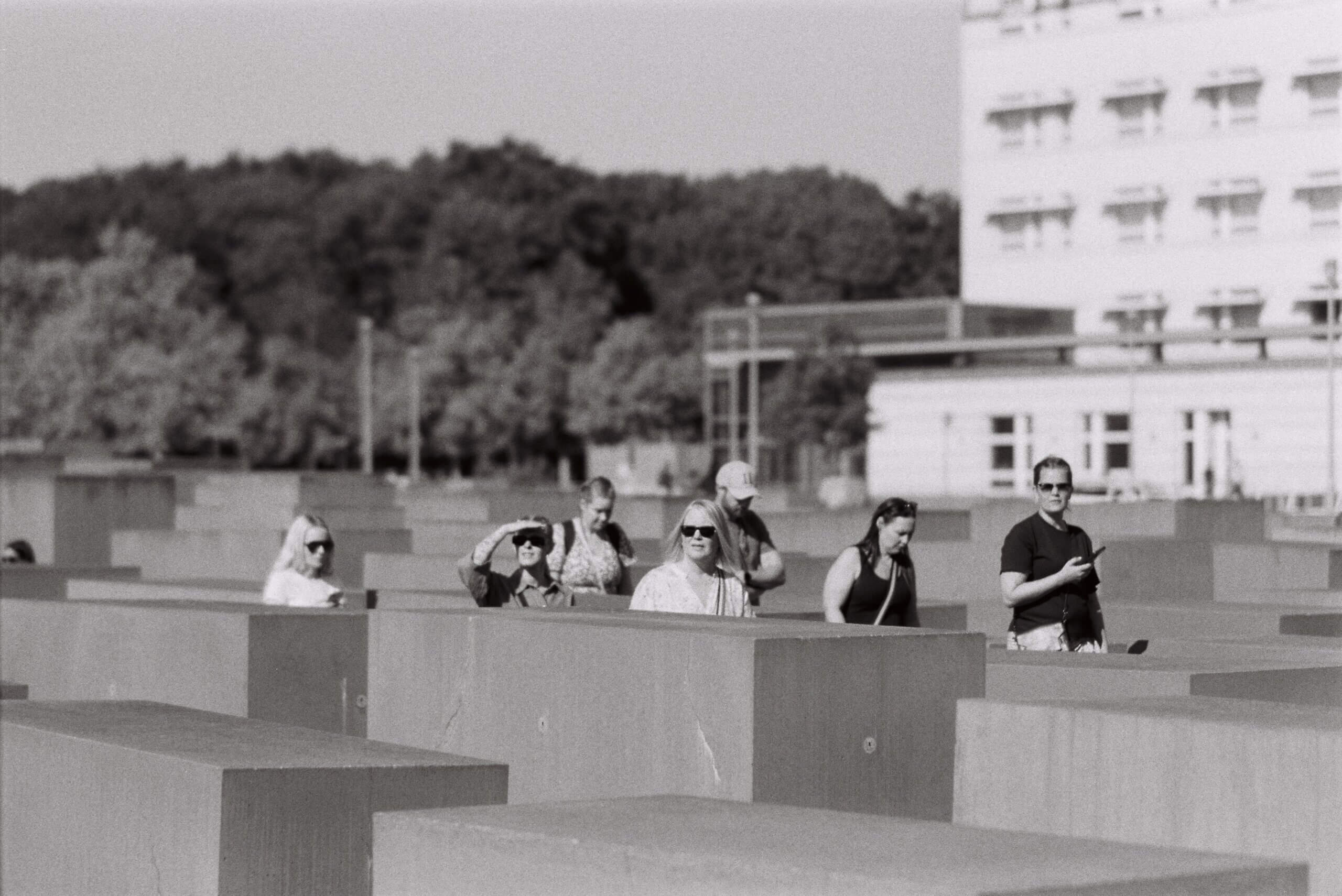 People wearing sunglasses and looking towards the sun walking through the stone slabs of Berlin's Memorial to the Murdered Jews of Europe.