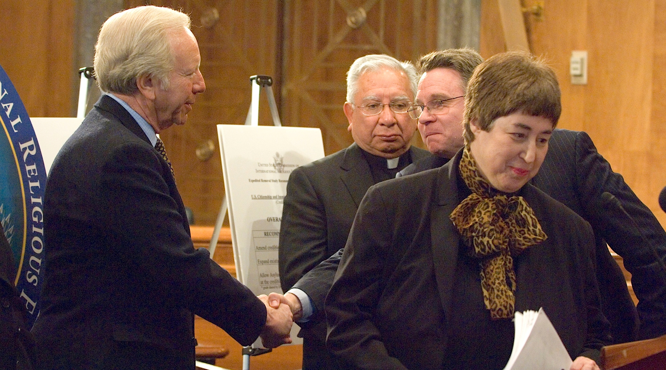 Felice Gaer, at right, then chair of the U.S. Commission on International Religious Freedom, takes part in a news conference presenting its report card on the two-year-old “Report on Asylum Seekers in Expedited Removal,” Feb. 7, 2007. At left, Sen.  Joseph Lieberman (D-Conn.) shakes hands with Rep. Chris Smith (R-N.J.) as Bishop Ricardo Ramirez, commissioner of the USCIRF, looks on. (Douglas Graham/Roll Call/Getty Images)