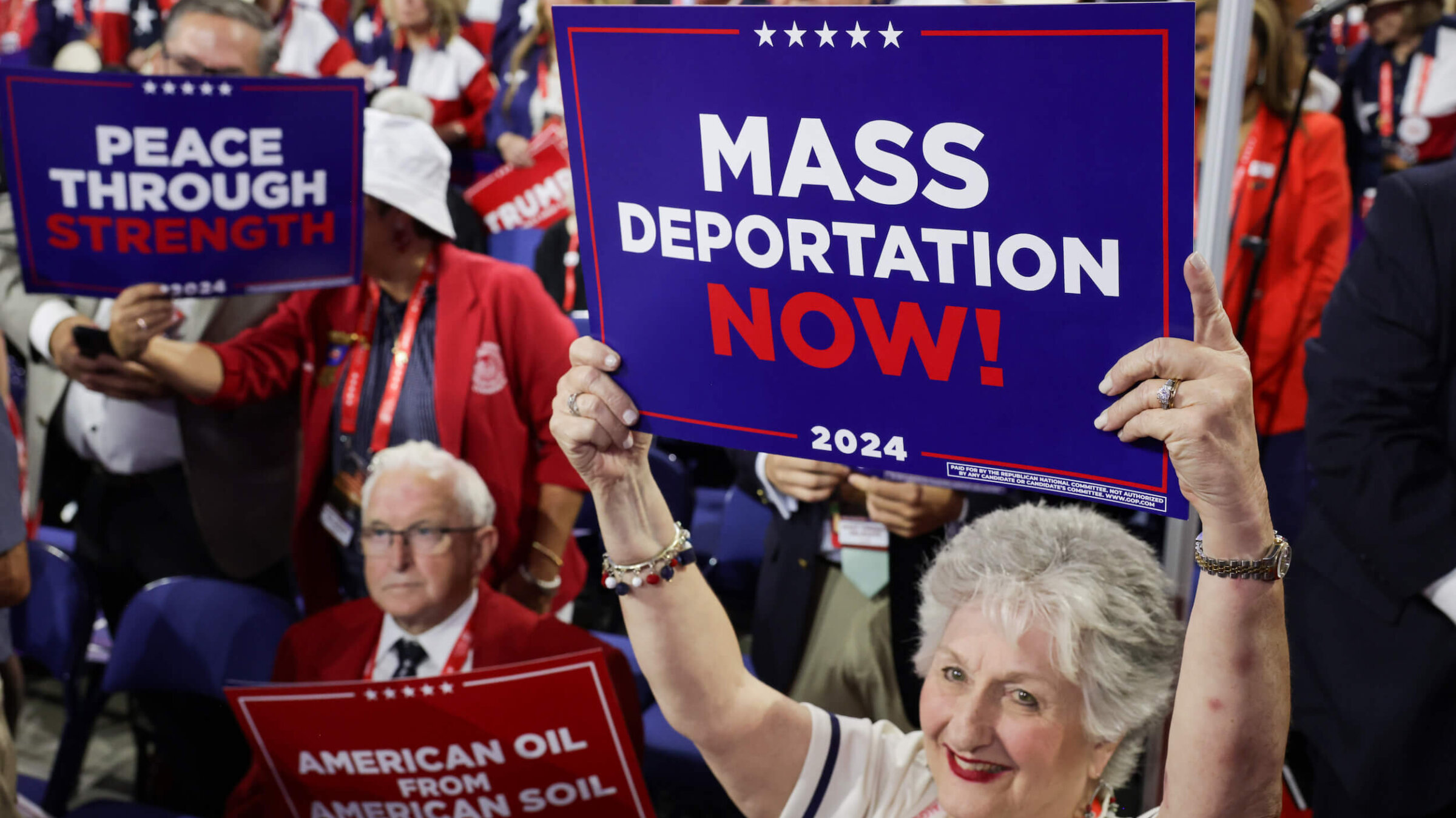 Attendees at the 2024 Republican National Convention hold signs reading "Mass Deportation Now!" 