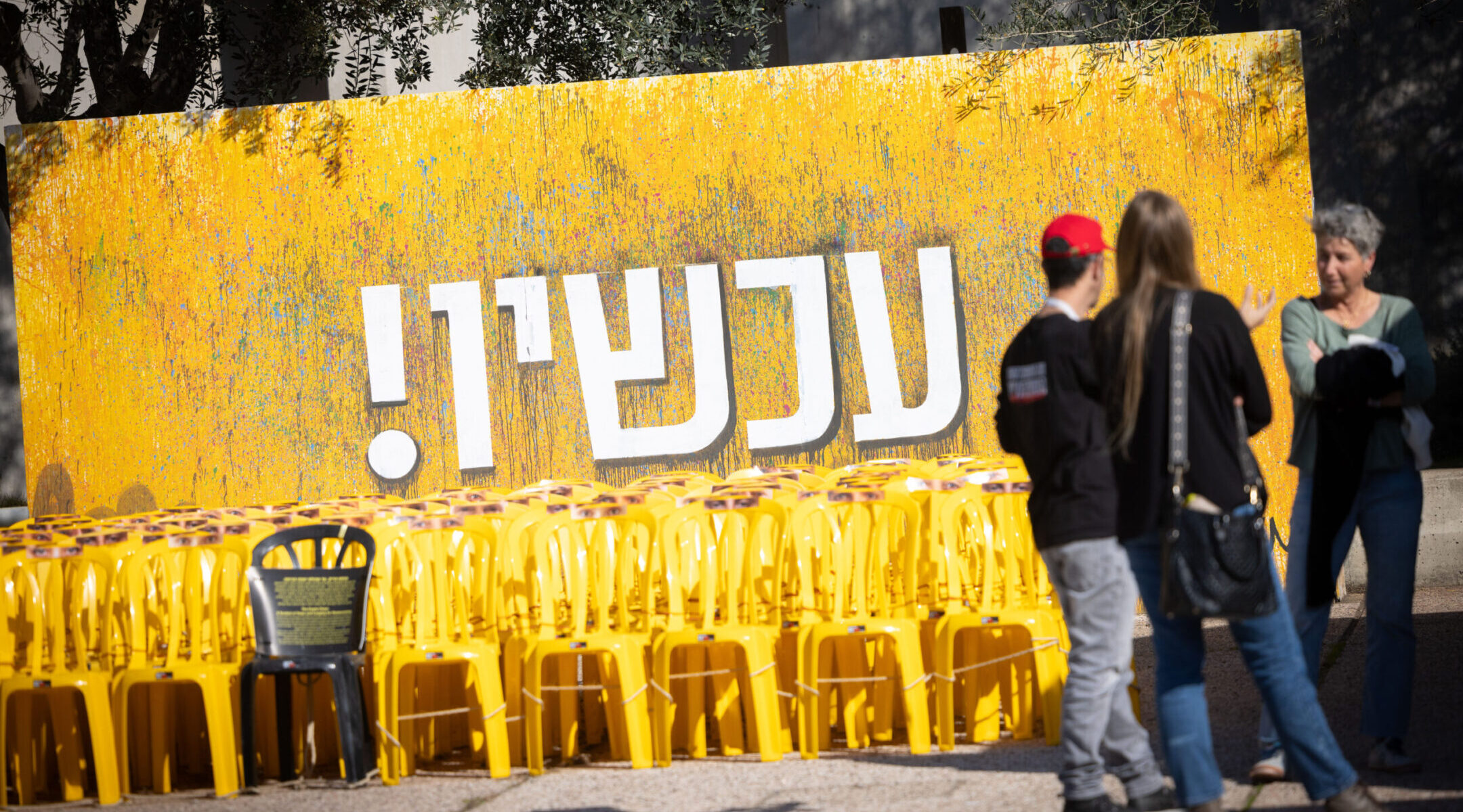 Visitors at Hostage Square in Tel Aviv stand in front of a sign reading “Now!” in Hebrew, Jan. 6, 2025. (Miriam Alster/Flash90)