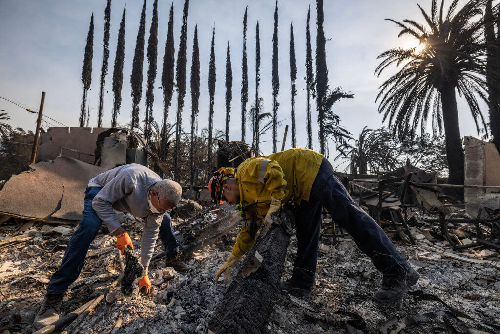 Rick Law (left) gets a helping hand from an LA County Firefighter as he digs throw rubble trying to recovery mementoes in the rubble of his Altadena home that burned to the ground  Jan. 10, 2024.