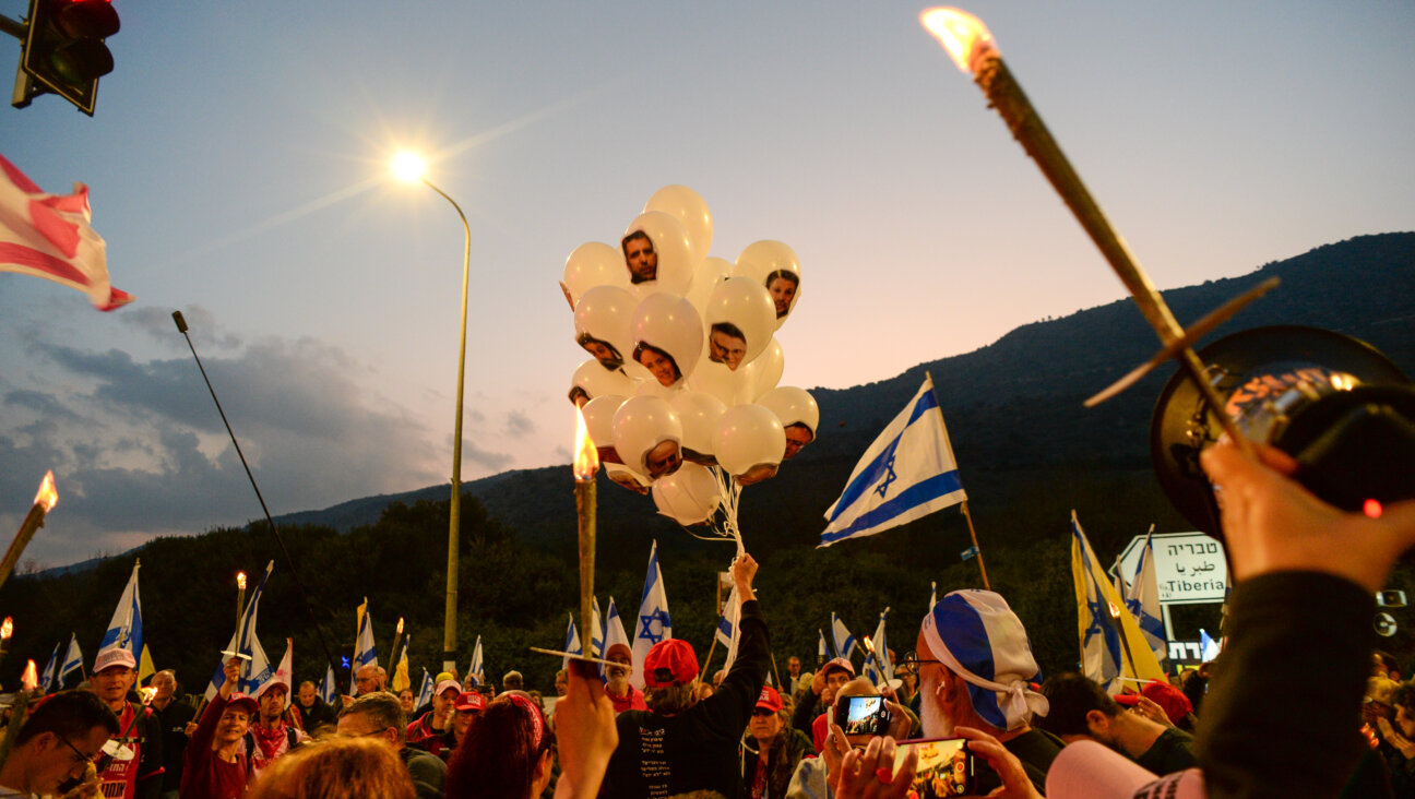 A demonstrator holds white balloons with the faces of Israeli Prime Minister Benjamin Netanyahu and his governing cabinet on them, while others carry torches and Israeli flags at a protest calling for an end to Israel's war in the Gaza Strip on January 11, 2025 in Kiryat Shmona, Israel.