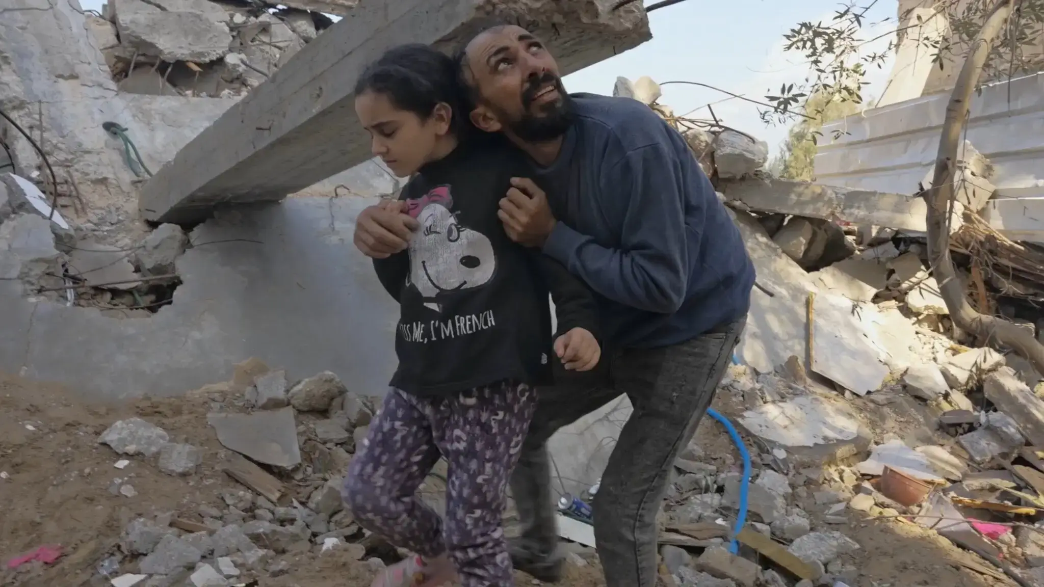 A man and his niece in Gaza pick through rubble, looking for her father, as bombs boom overhead.