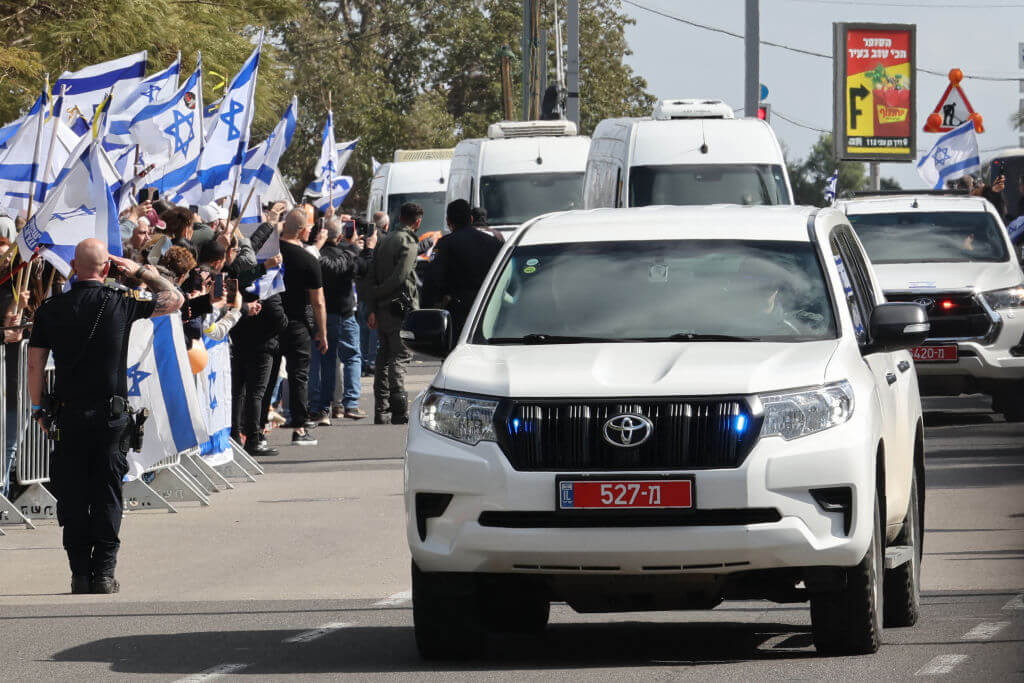 Israelis wave the national flag as the convoy of vehicles transporting the bodies of the four Israeli hostages handed over by Hamas, including the Bibas family, arrives at the entrance to the National Center of Forensic Medicine in Tel Aviv on February 20. 