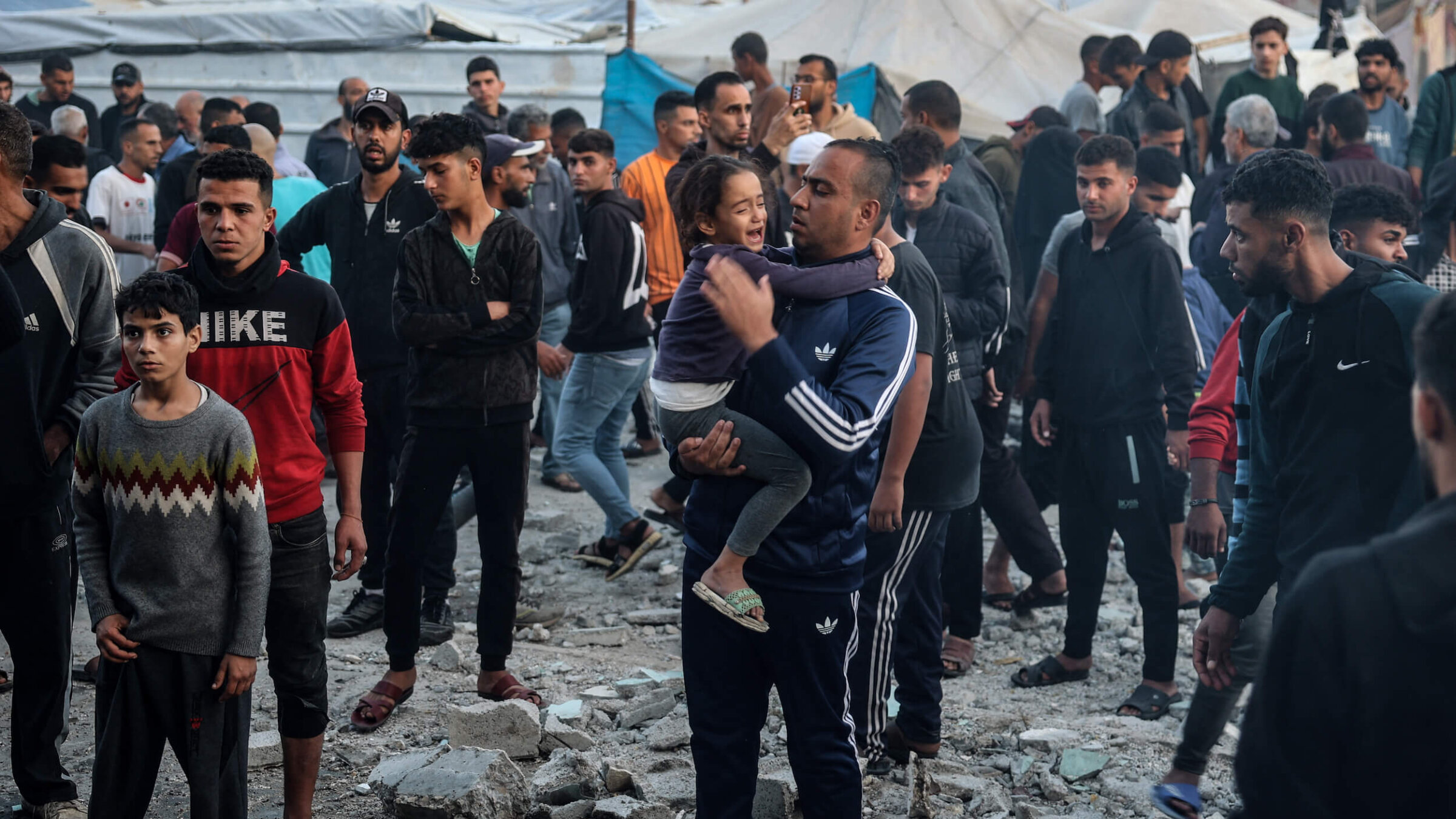 A man holds a crying child as displaced Palestinians check the destruction following an Israeli strike that hit a UN-run school, in the central Gaza Strip on Nov. 20, 2024. 